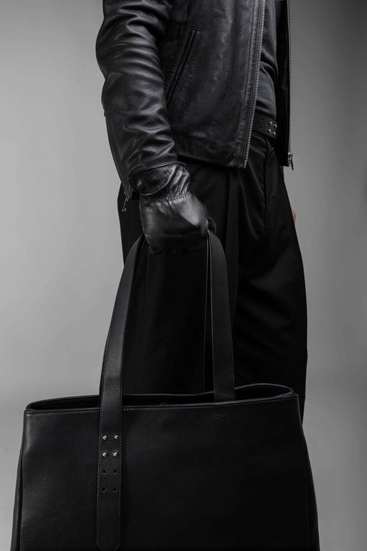 Close up of a man carrying a leather tote bag wearing black leather gloves