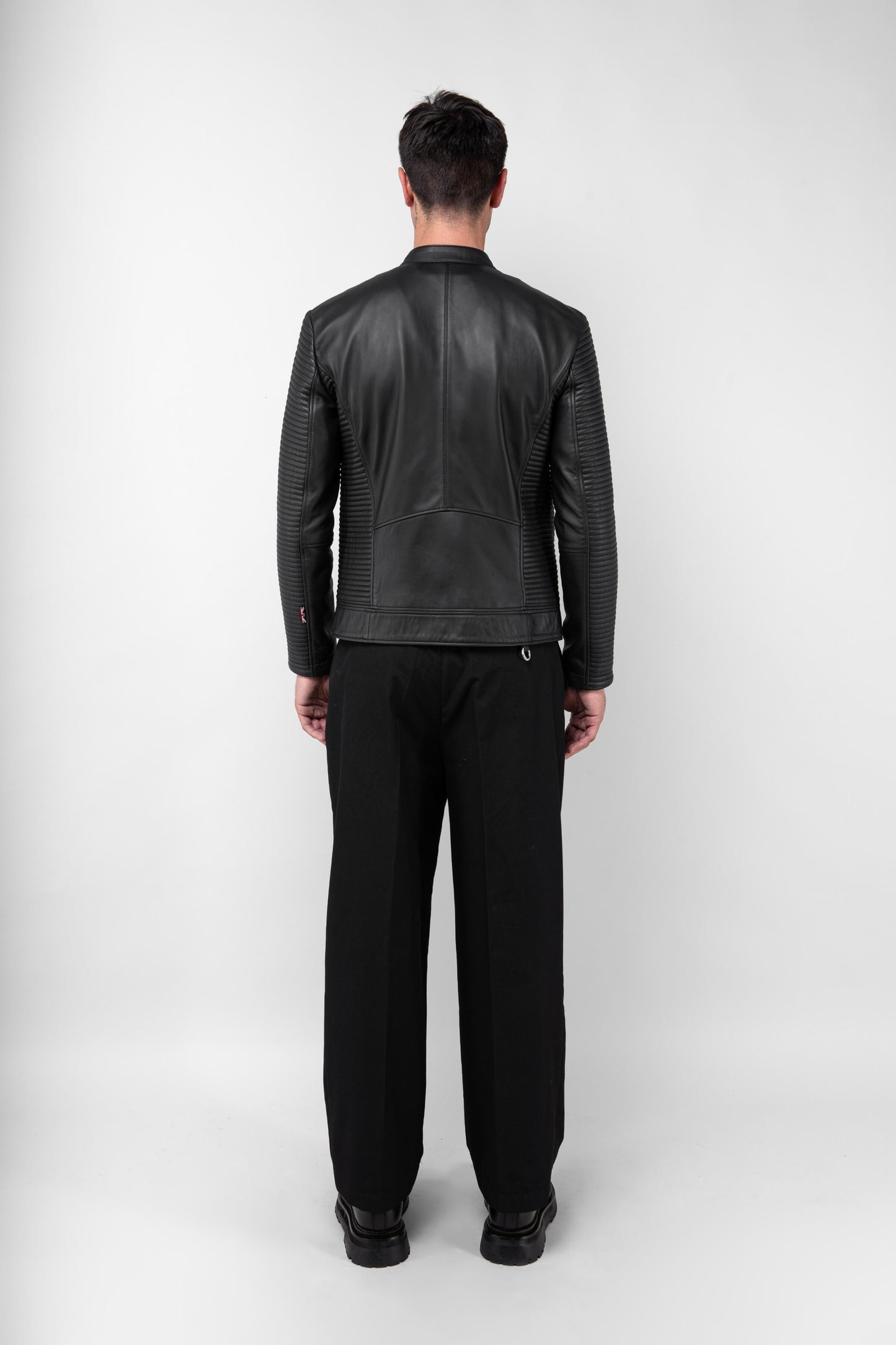 Back view of a male model wearing a collarless black Leather Jacket in a tall size, tailored fit, and sleeve detailing.a
